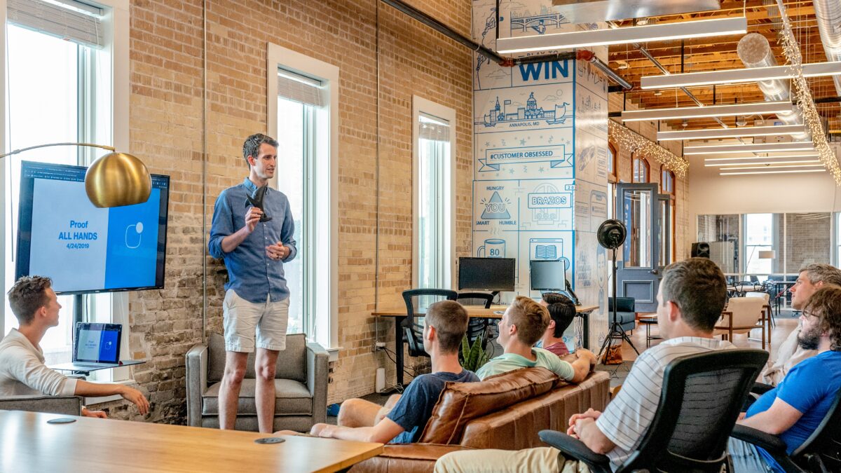 a small audience of young adults listening to one student present in a loft-style space.