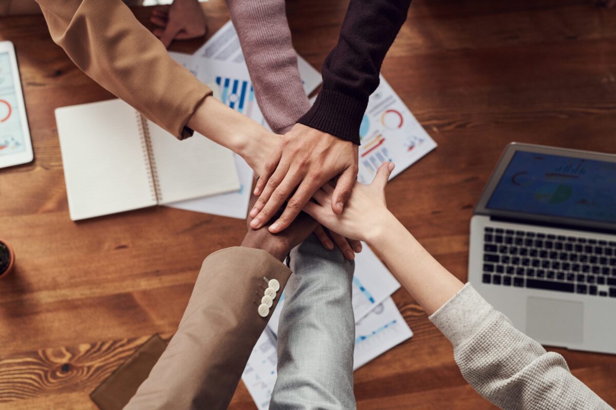 6 individuals put their hands in the middle of their circle. Only hands and forearms are visible.