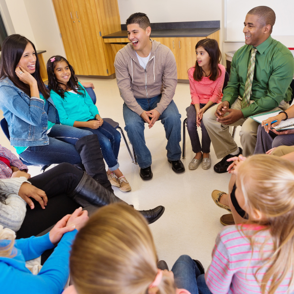A group of students and teachers are sitting in a circle on chairs having a conversation.